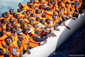 Rubber boat filled with migrants wearing lifejackets.