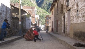 Dos niños jugando al toro con un poncho, a falta de un capote.